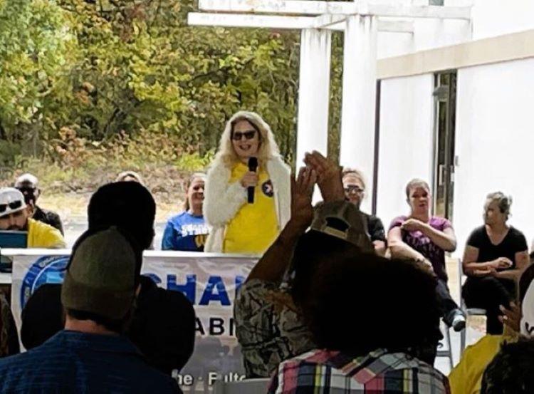 Person speaking at outdoor event, audience applauding.