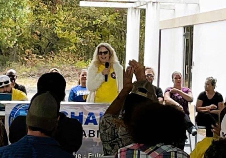 Person speaking at outdoor event, audience applauding.